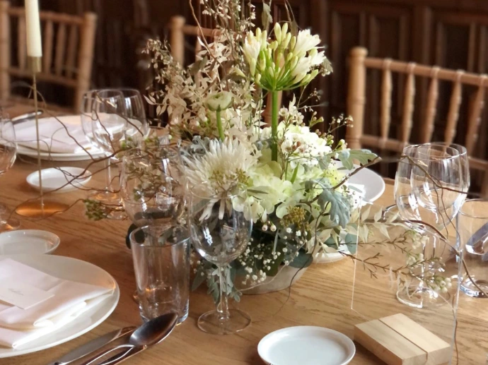 Elegant wit bloemstuk in een glazen vaas op een gedekte houten tafel.