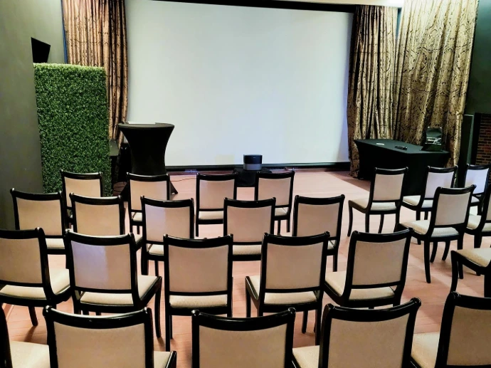 Professionele zaalopstelling met rijen stoelen gericht op een groot projectiescherm.